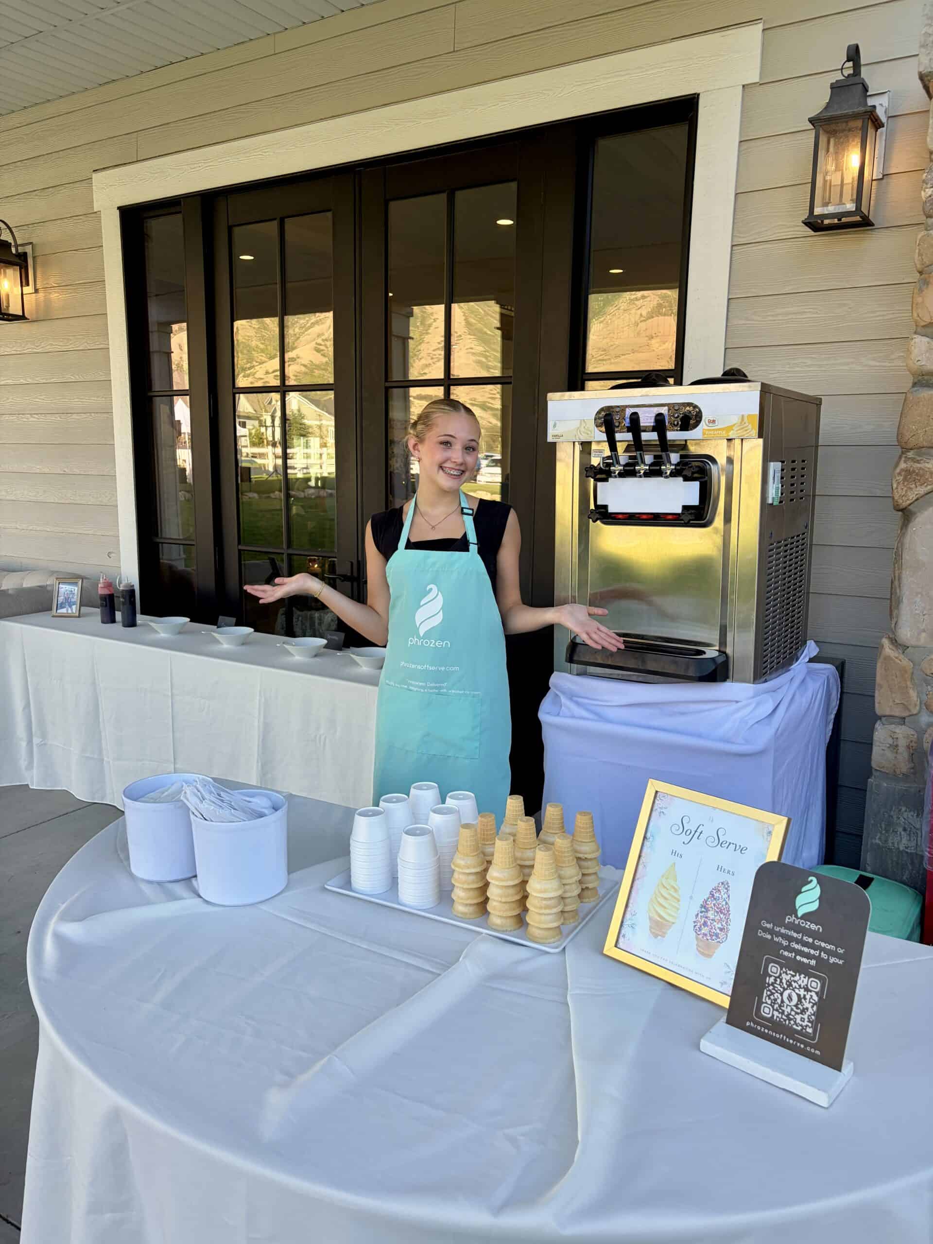 A Phrozen Soft Serve attendant in a teal apron beside the machine, cones and toppings on the covered patio at Northridge Valley in Mapleton