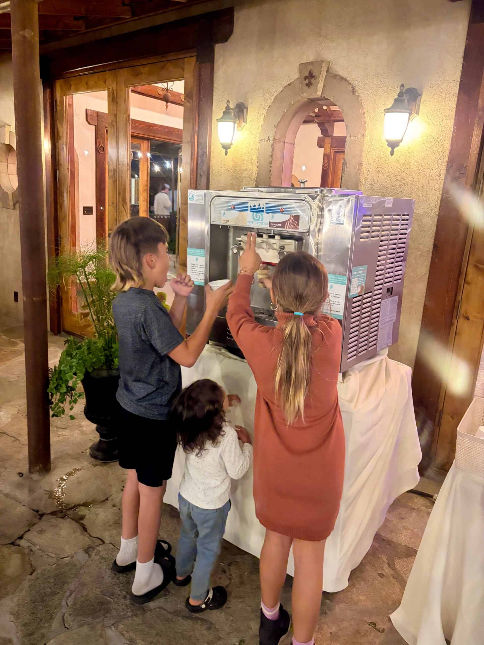 Three children helping themselves at the soft serve machine in the stone courtyard at Wadley Farms in Lindon