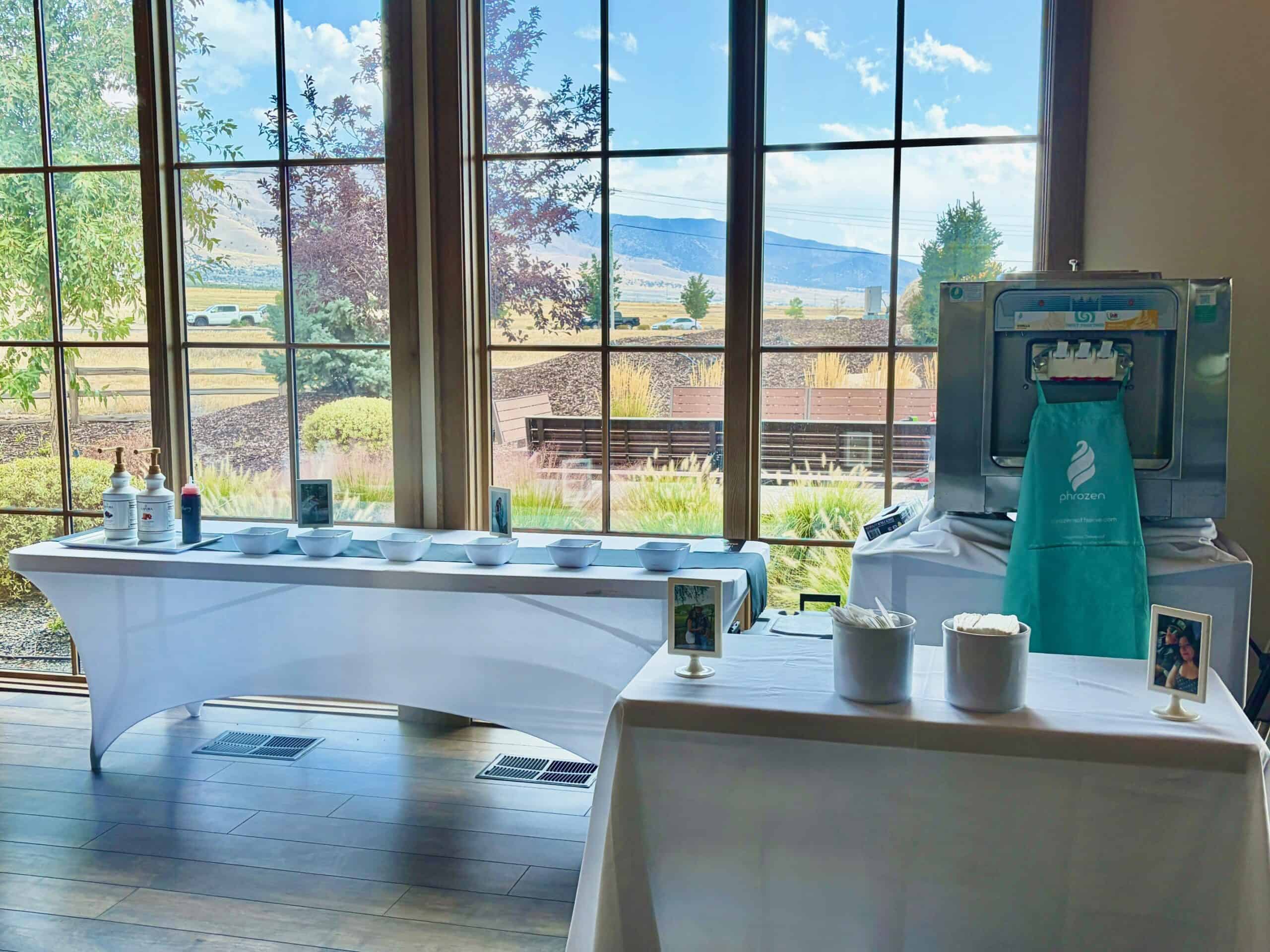 A soft serve machine and toppings table set up in front of floor-to-ceiling windows with mountain views at the Barn at Overland in Eagle Mountain